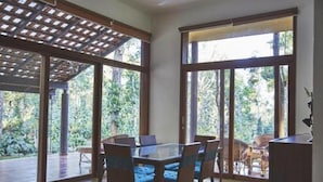 A dining area with a glass table and chairs, large windows, and a wooden ceiling structure.