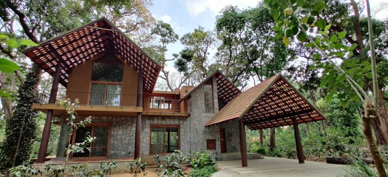 A two-story house with a stone facade, large windows, and a wooden pergola structure.