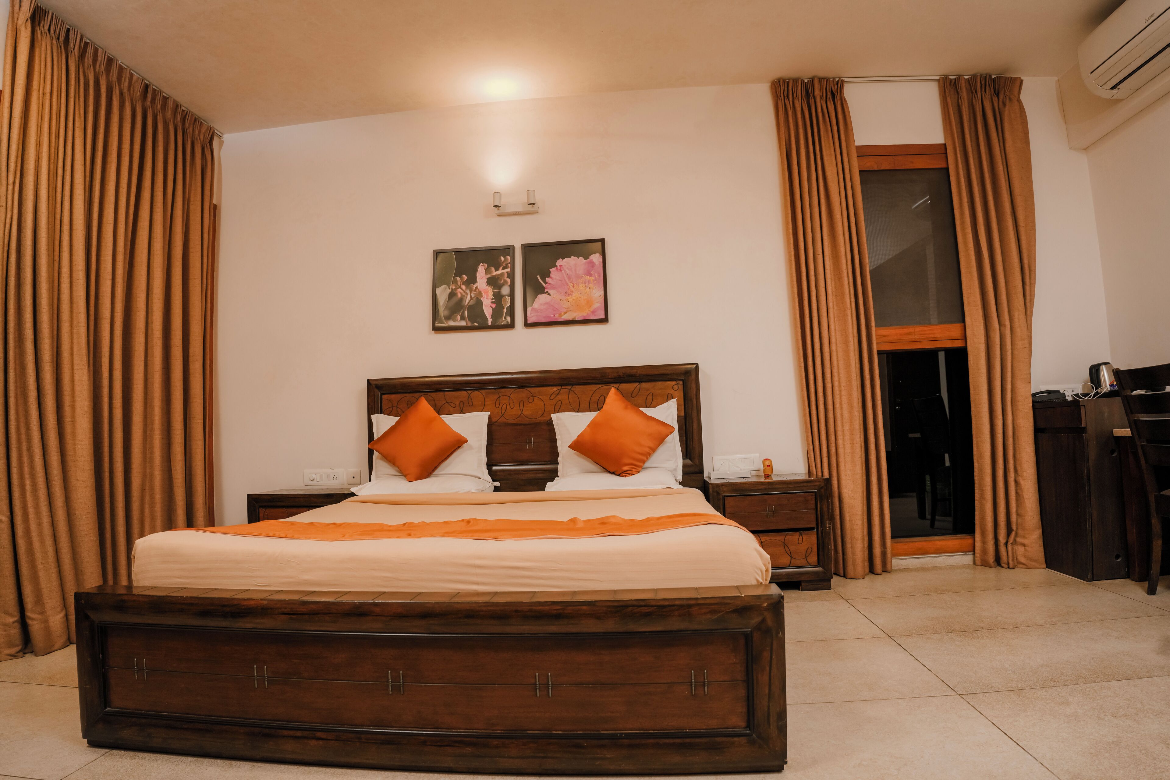 Habitación de hotel con una cama grande, cabecero de madera, dos mesitas de noche, un escritorio y una ventana con cortinas.