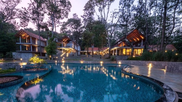 A swimming pool with a tiled edge, surrounded by a stone deck and a wooden pergola.