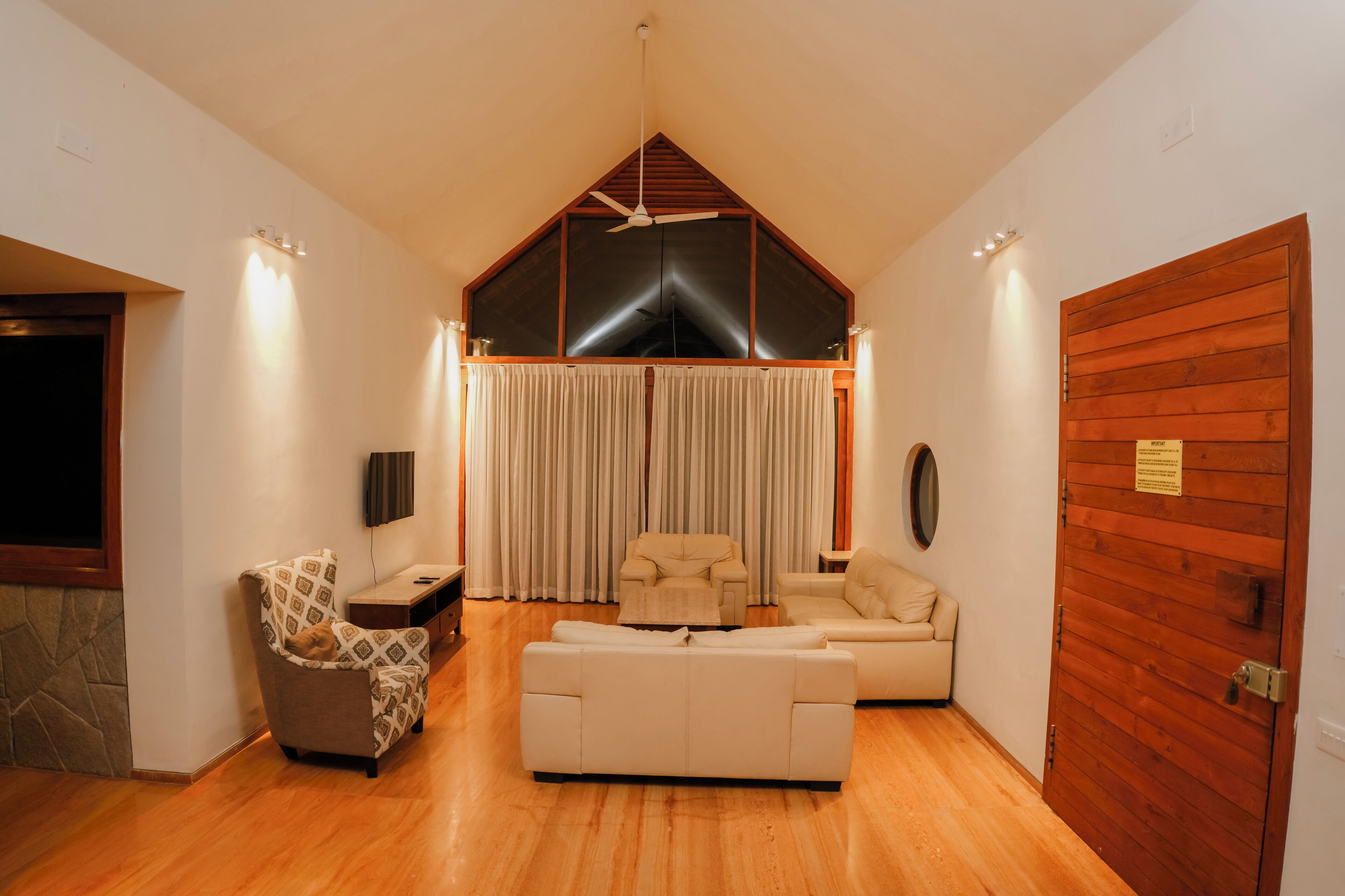 A spacious living room with a high ceiling, a wooden door, and a large window.