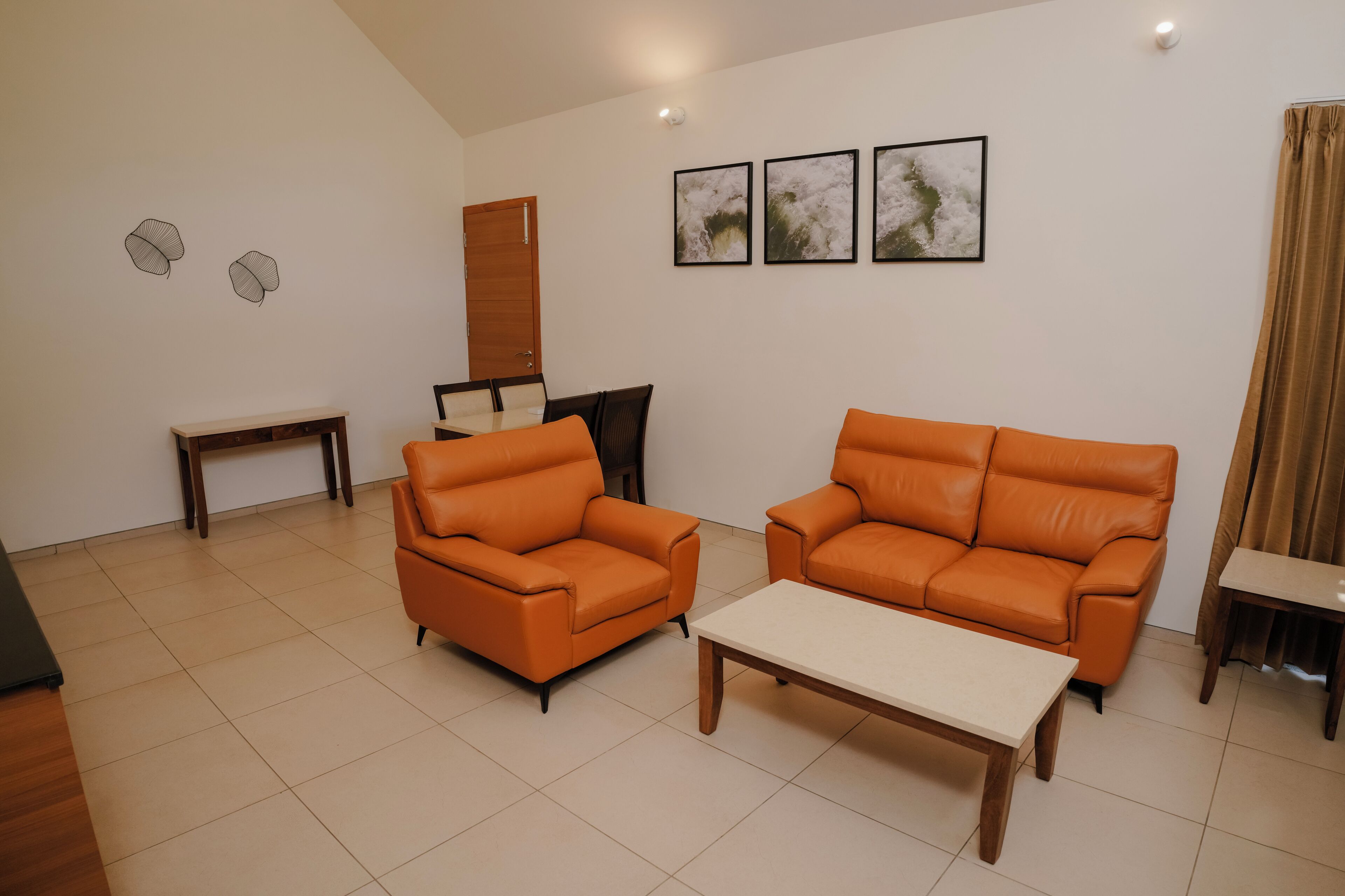 A living room with two orange sofas, a coffee table, and a small table. There are three framed pictures on the wall.