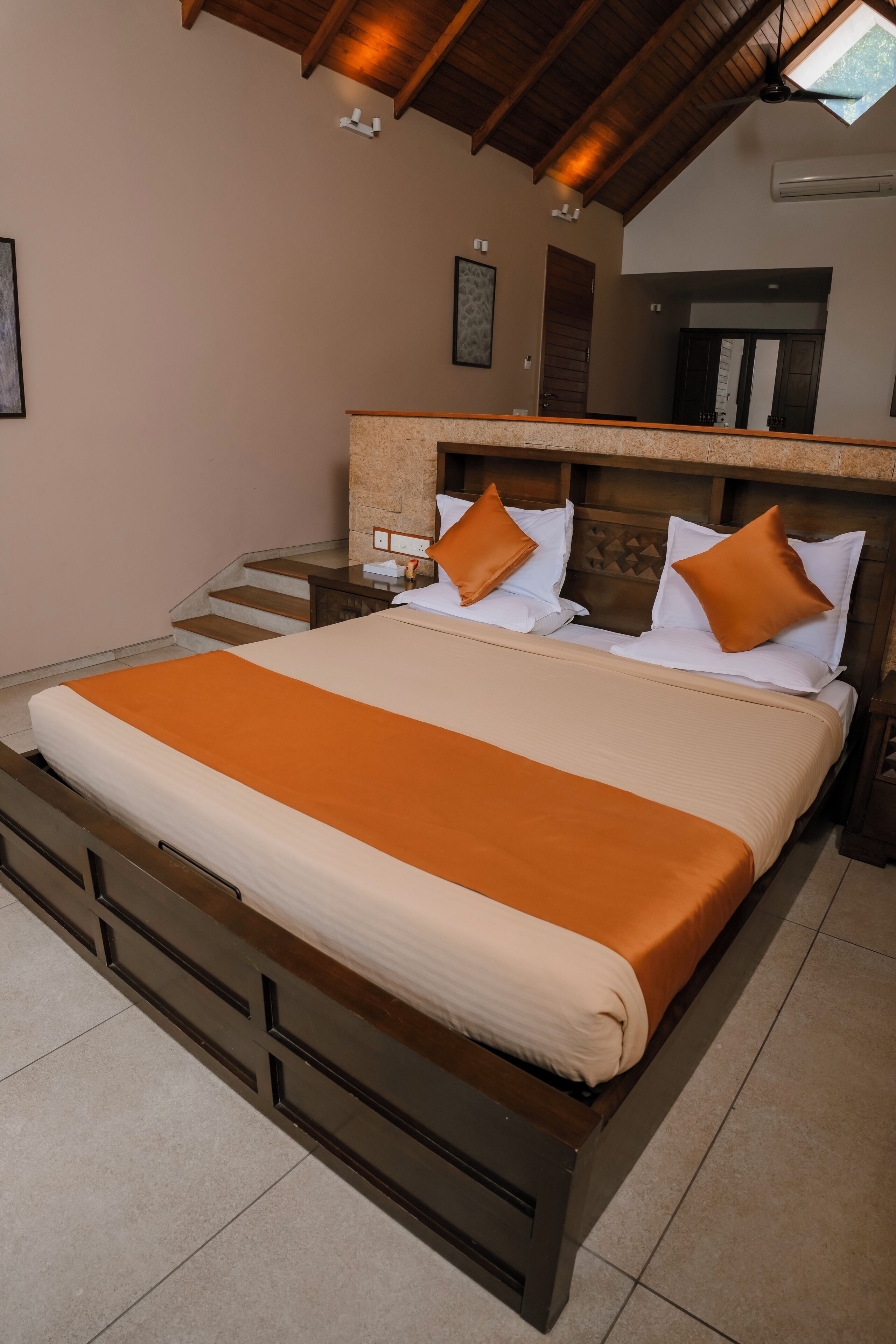 A bedroom with a large bed, wooden headboard, and a staircase leading to an upper level.