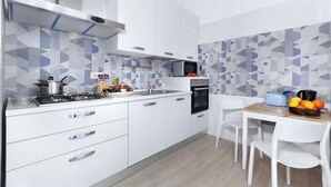 A modern kitchen with white cabinets, a gas stove, a microwave, and a toaster. There is a wooden table with chairs and a bowl of fruit. - Casa Marevista in Sorrento centre (Sorrento)