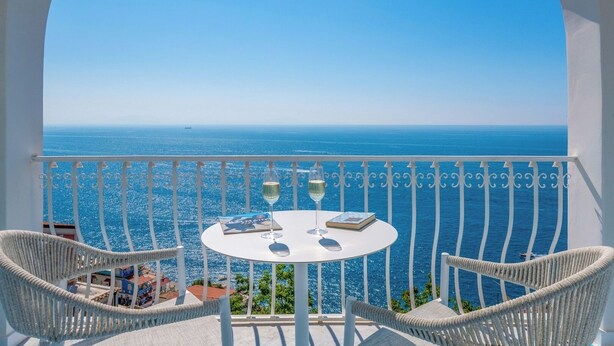 A balcony with a white table and chairs, overlooking a clear blue sea. - Villa Pelagium on the Amalfi Coast (Praiano)