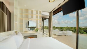 A modern hotel room with a large bed, a round mirror, a vanity with a mirror, and a balcony with outdoor seating.