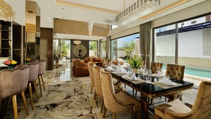 A modern dining area with a marble floor, a long table set for dining, and a view of the sea through large windows.