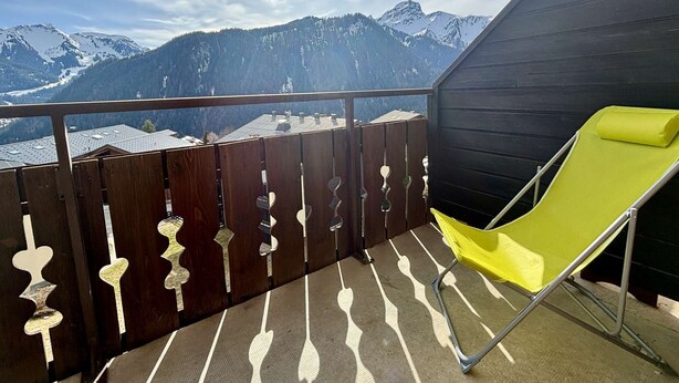 A balcony with a yellow chair, wooden railing, and a mountain view. - Yéti 3 - T3 + Mezzanine (CHATEL)