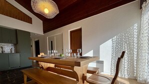 A modern kitchen with wooden cabinetry, a dining area with a wooden table and benches, and a large window with lace curtains. - Yéti 3 - T3 + Mezzanine (CHATEL)