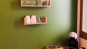 Una cocina con estantes de madera que sostienen cristalería y tazas, una cafetera y una caja sobre la encimera.