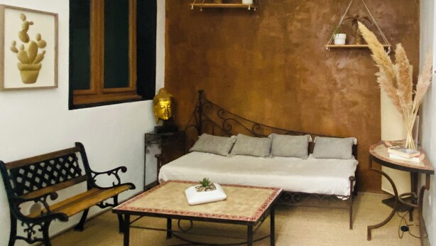 Un cuarto acogedor con una cama, un banco, una mesa y un estante con plantas.