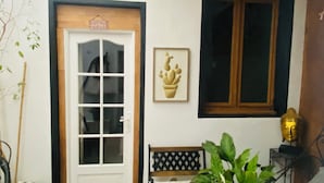 Una puerta con un letrero que dice 'Welcome to Patio', una obra de arte con un cactus enmarcado, una ventana y un banco con una planta en maceta a su lado.