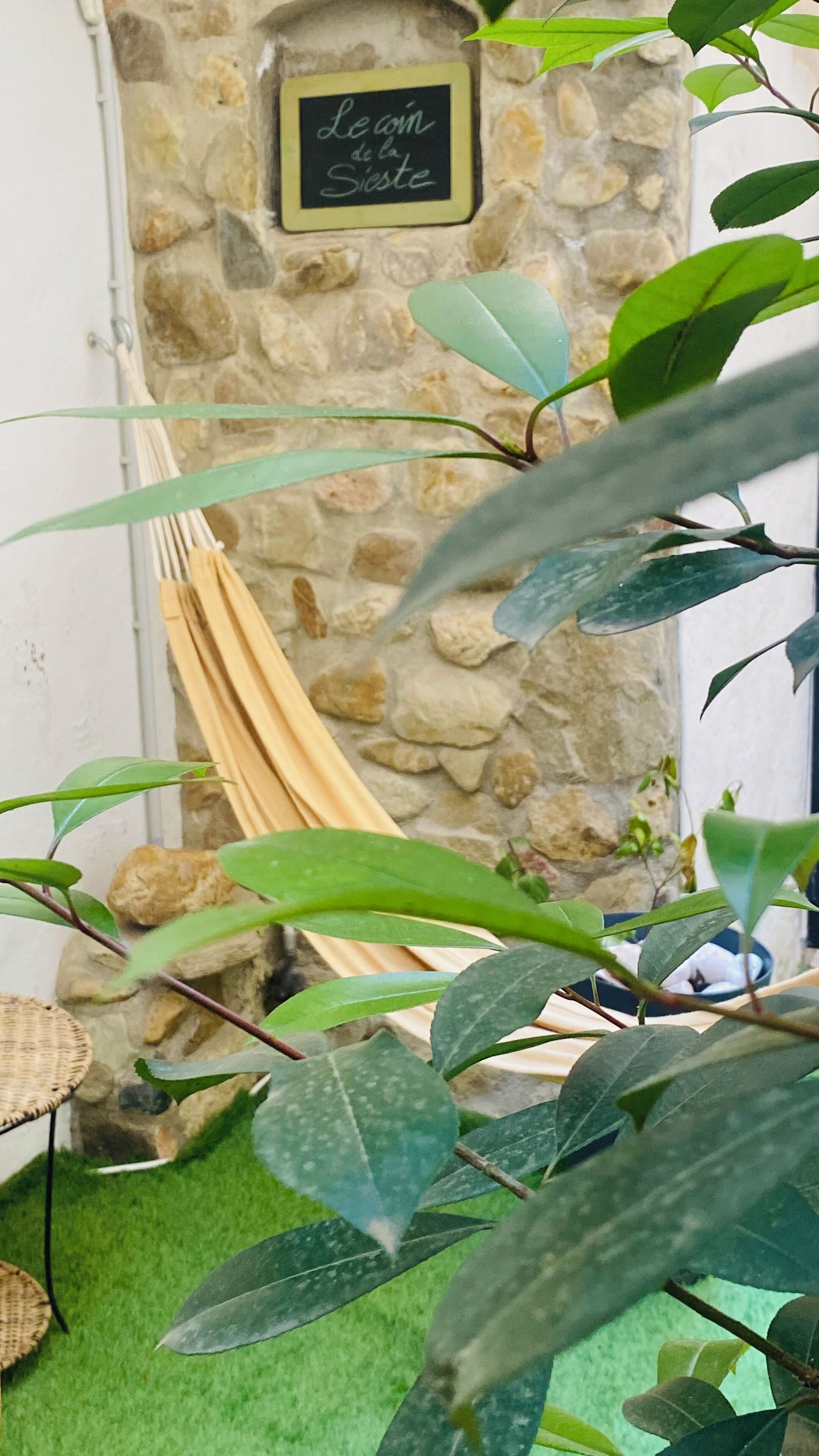 A stone wall with a sign reading "Le coin de la Sieste" and a hammock.