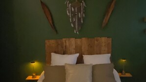 Una cama con sábanas blancas y varios almohadones, cabecera de madera y un atrapasueños en la pared.