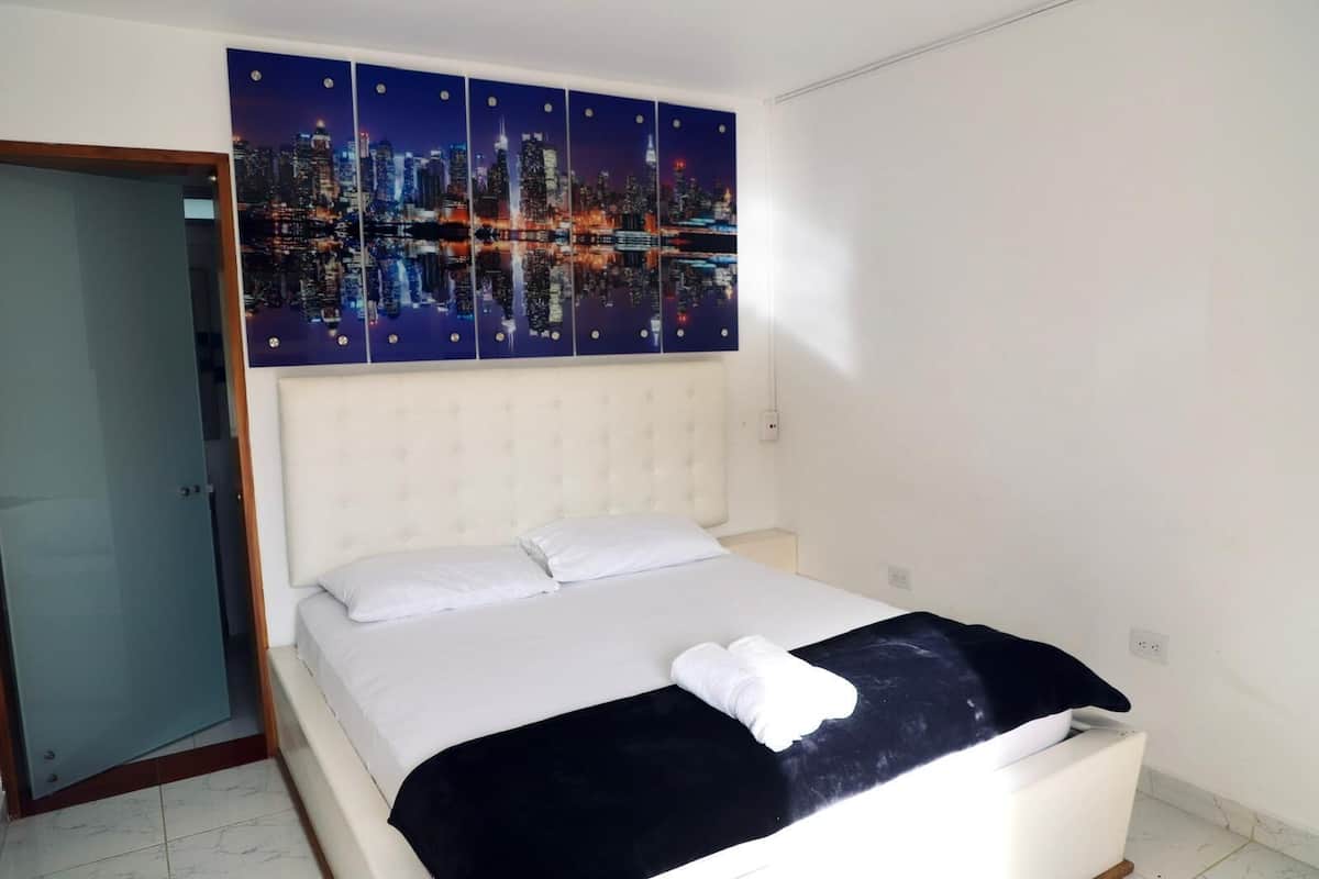 A hotel room with a large bed, a cityscape artwork above the bed, and a white headboard.