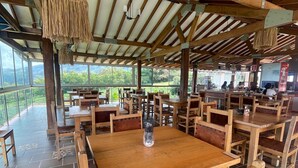 A restaurant with wooden tables and chairs, a hanging light fixture, and a view of the outdoors. - Mountain View (Girardota)