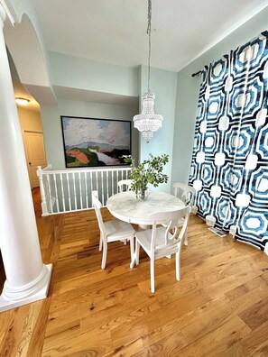 A dining area with a white table and chairs, a chandelier, and a patterned curtain.