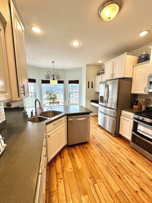 A modern kitchen with a dishwasher, refrigerator, stove, and wooden flooring.