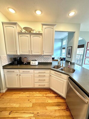 A kitchen with white cabinets, a black countertop, a stainless steel sink, and a dishwasher. - 6BR Ephraim, UT Home - 11 Beds, Tesla Charger, ATV Trails, Near Snow College (Ephraim)