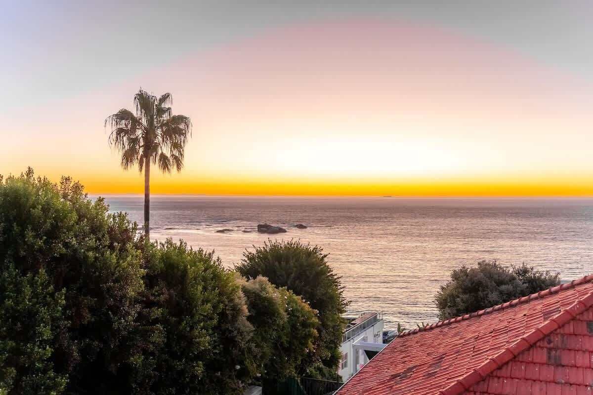 Vista costeira com palmeira, oceano e um edifício de telhado vermelho.