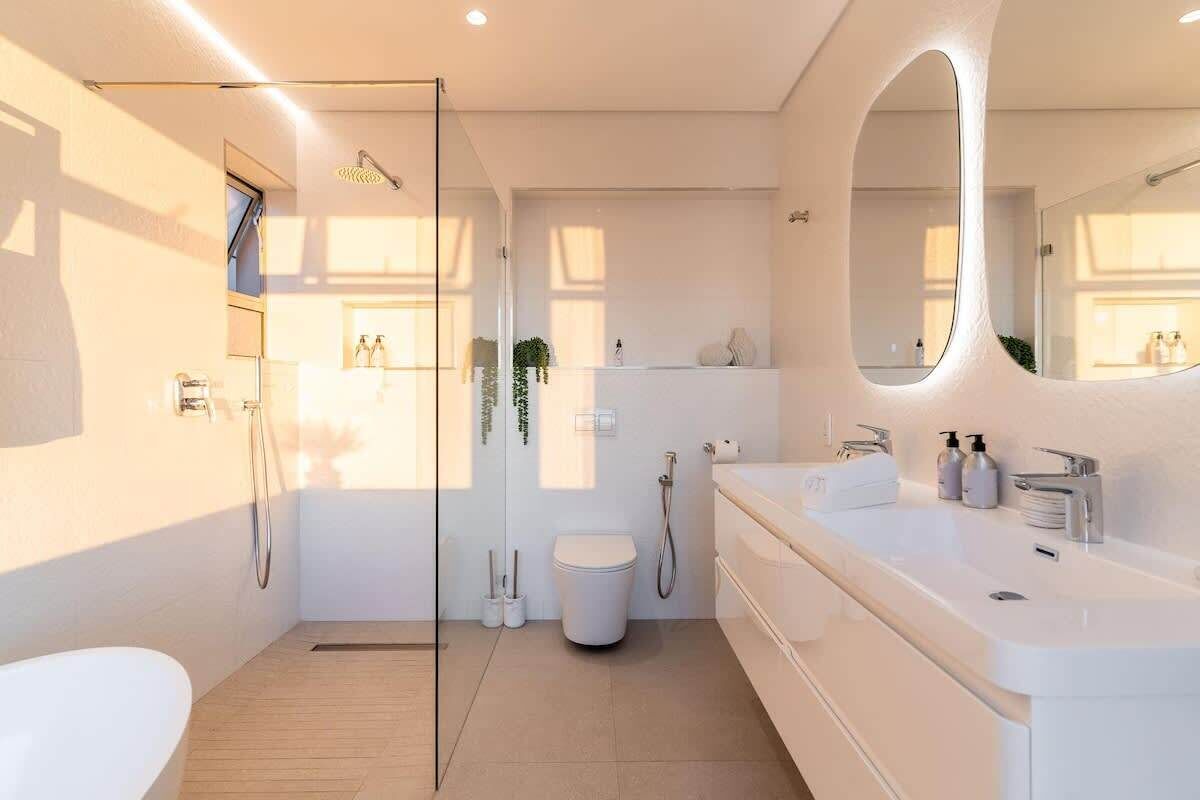 A modern bathroom with a glass shower enclosure, a large mirror, and a white sink.