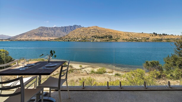 Un coin repas avec une table dressée pour deux personnes, donnant sur un lac et offrant une vue sur des montagnes en arrière-plan.