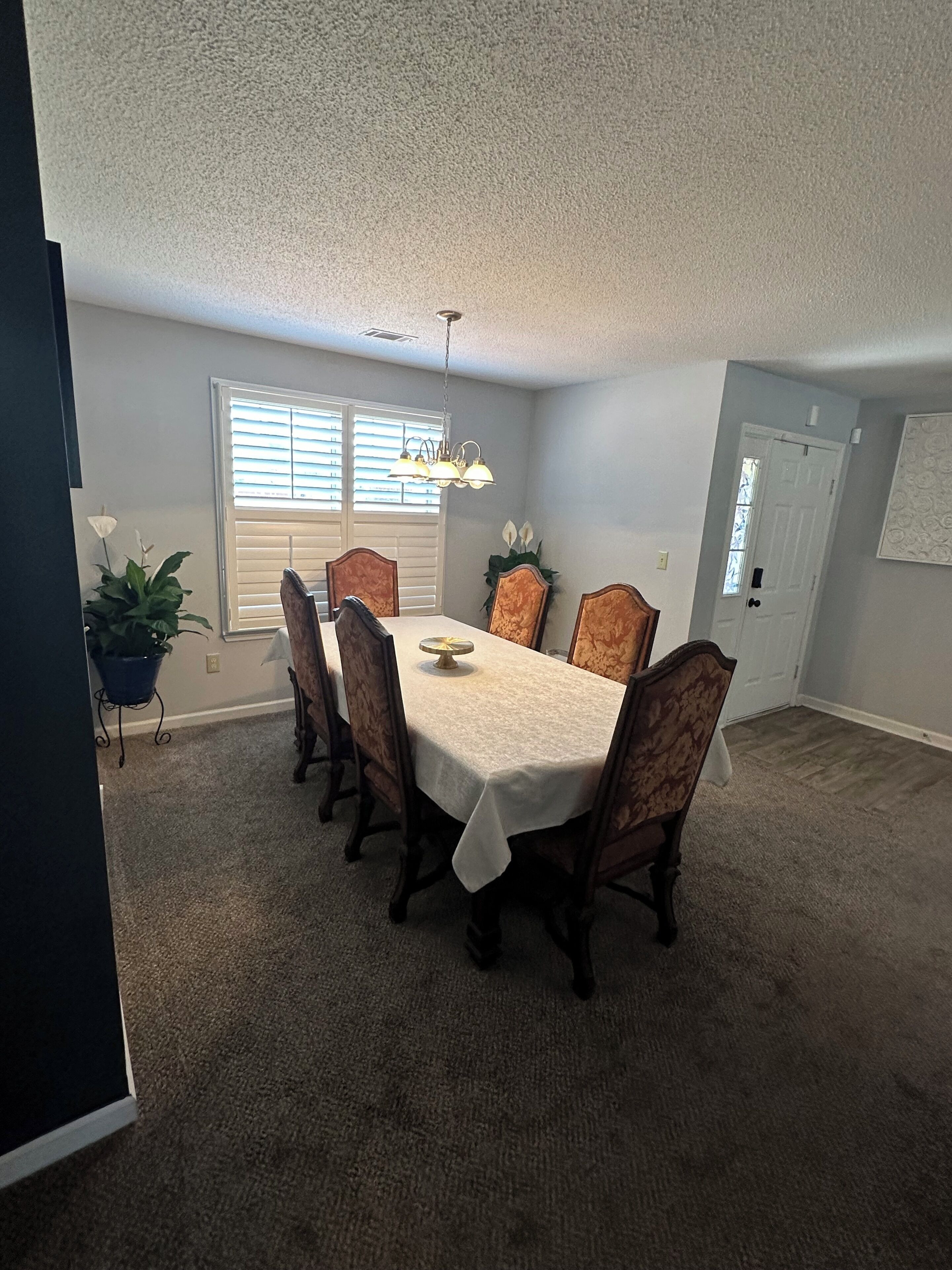 A dining room with a table set for four, surrounded by chairs, a ceiling fan, and a window with blinds.