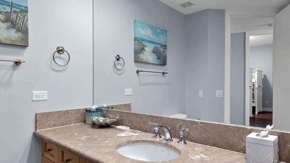 A bathroom with a large mirror, a sink, and two towel rings. There are two paintings on the wall. - 3rd Coast Getaways - Sapphire 803 (South Padre Island)