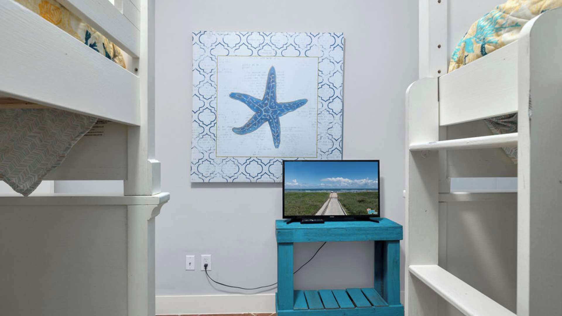 Una habitación con literas, un televisor sobre un soporte azul y una obra de arte con forma de estrella de mar en la pared.