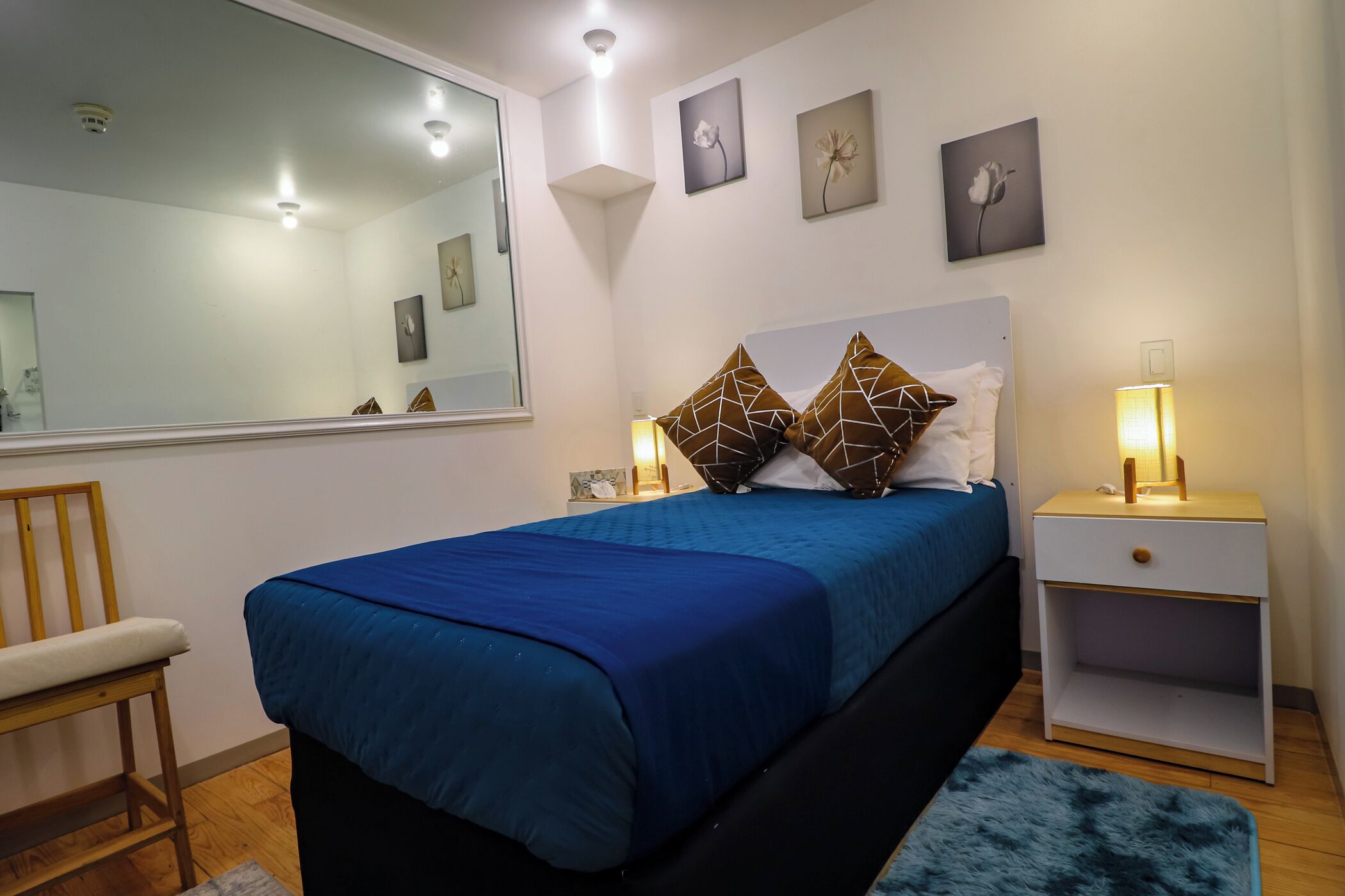 A bedroom with a bed, bedside table, lamp, and a mirror.