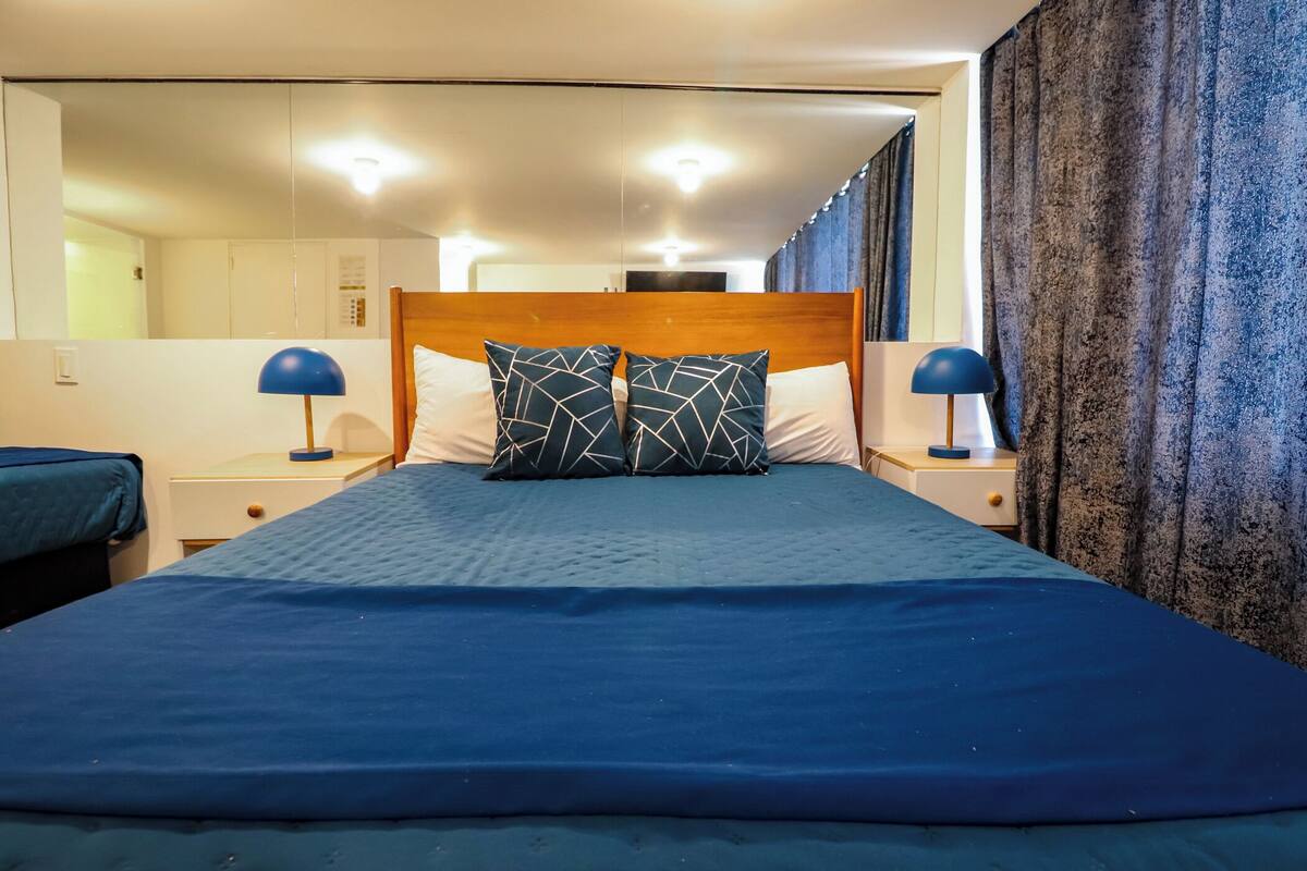 A hotel room with a large bed, two bedside tables with lamps, a headboard, and a mirror.