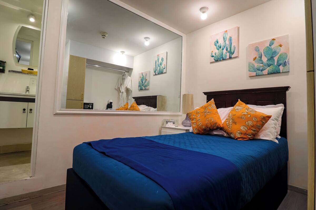 A bedroom with a large bed, a nightstand, a mirror, and artwork on the wall.