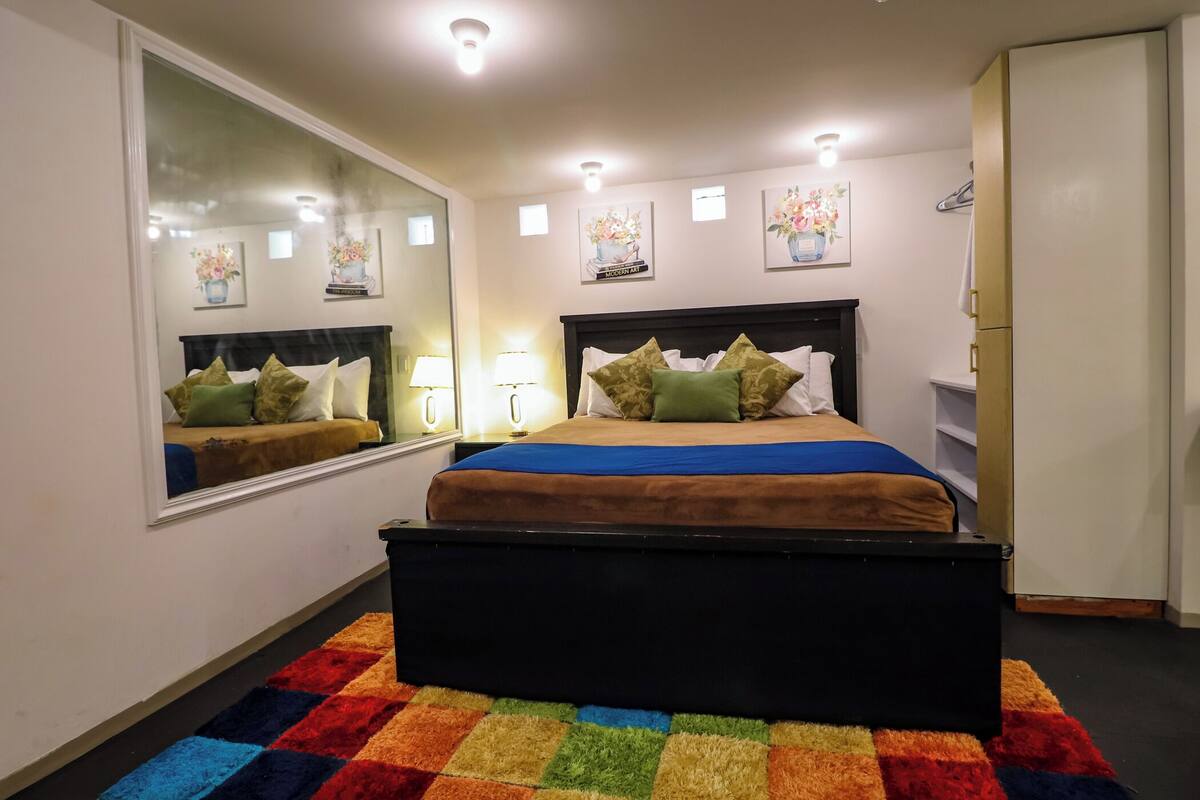A bedroom with a bed, a large mirror, bedside lamps, and a colorful rug.