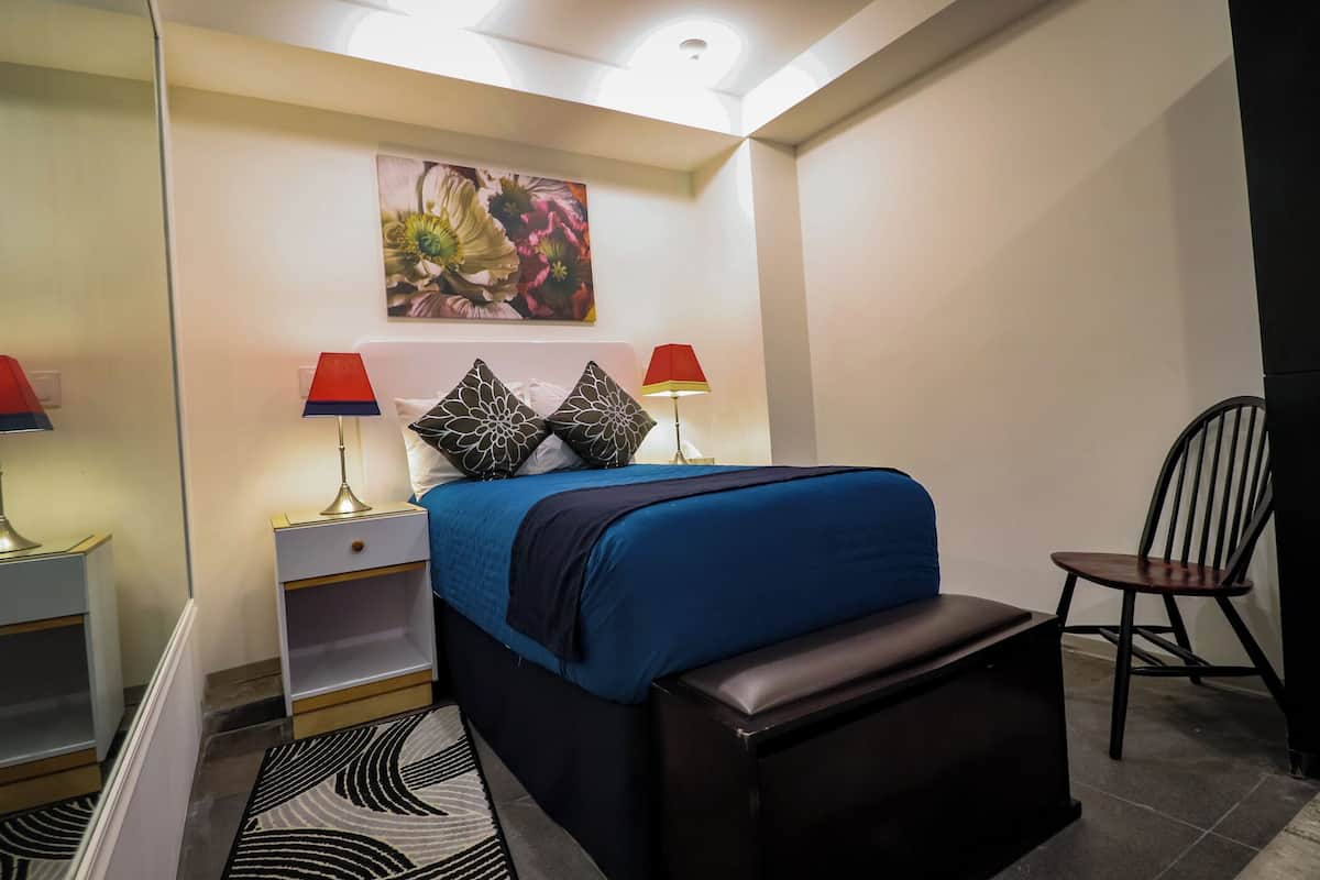 A bedroom with a bed, two nightstands, a chair, and a painting on the wall.