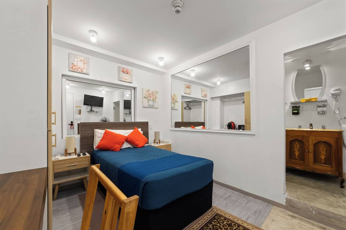 A modern hotel room with a large bed, a wooden nightstand, a mirror, and a wardrobe.