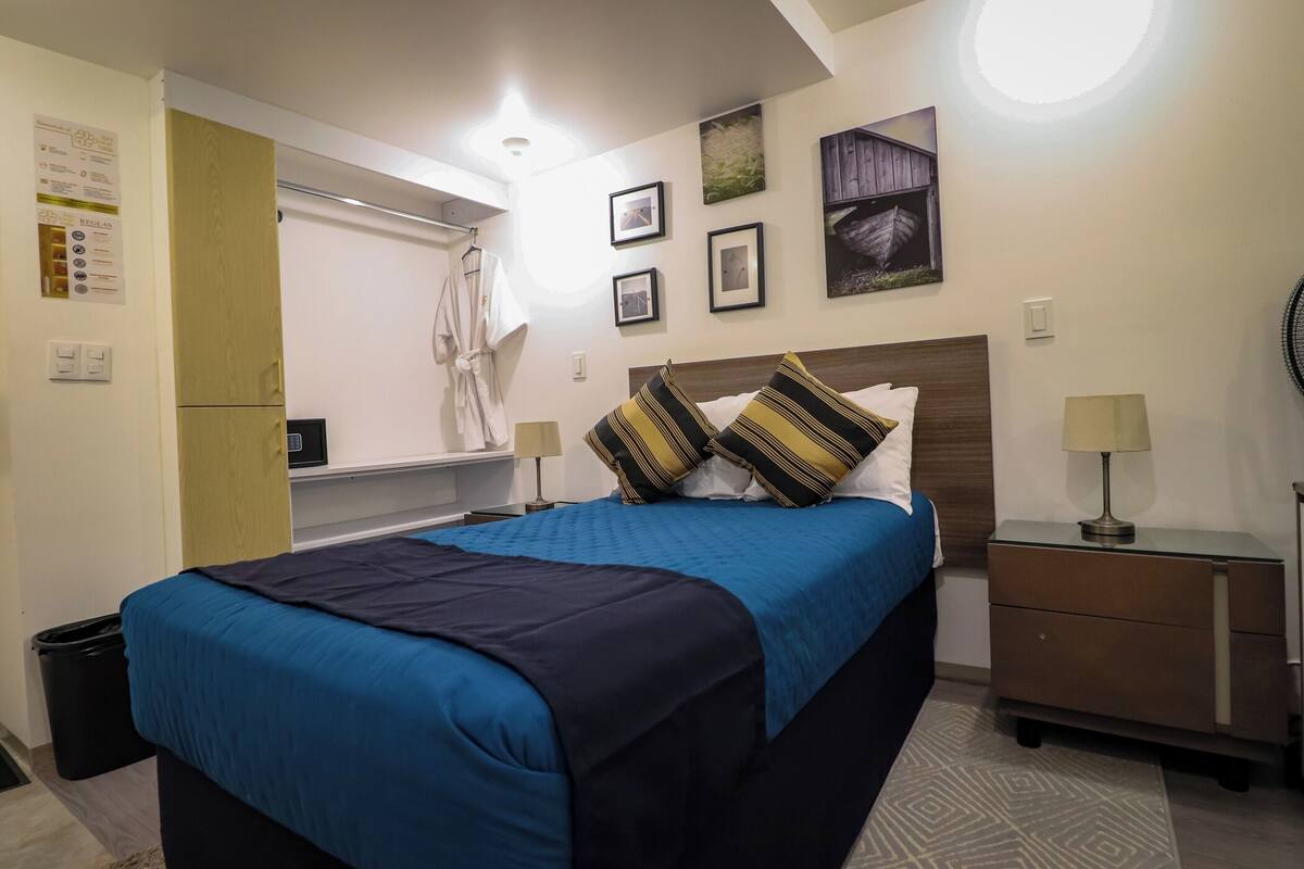 A neatly arranged hotel room with a bed, bedside tables, a wardrobe, and a small desk.