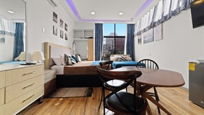 A modern bedroom with a bed, bedside table, dresser, and a dining table with chairs. - Hotel Boutique Emma  (Mexico City)