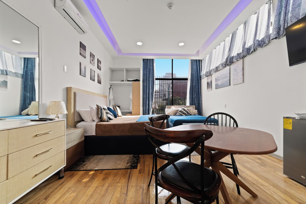 A modern bedroom with a bed, bedside table, dresser, and a dining table with chairs.