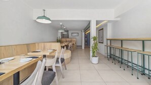 A modern dining area with wooden tables and chairs, green pendant lights, and a potted plant. - Hotel Boutique Emma  (Mexico City)