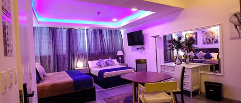 A modern hotel room with a bed, a desk, a chair, and a TV.