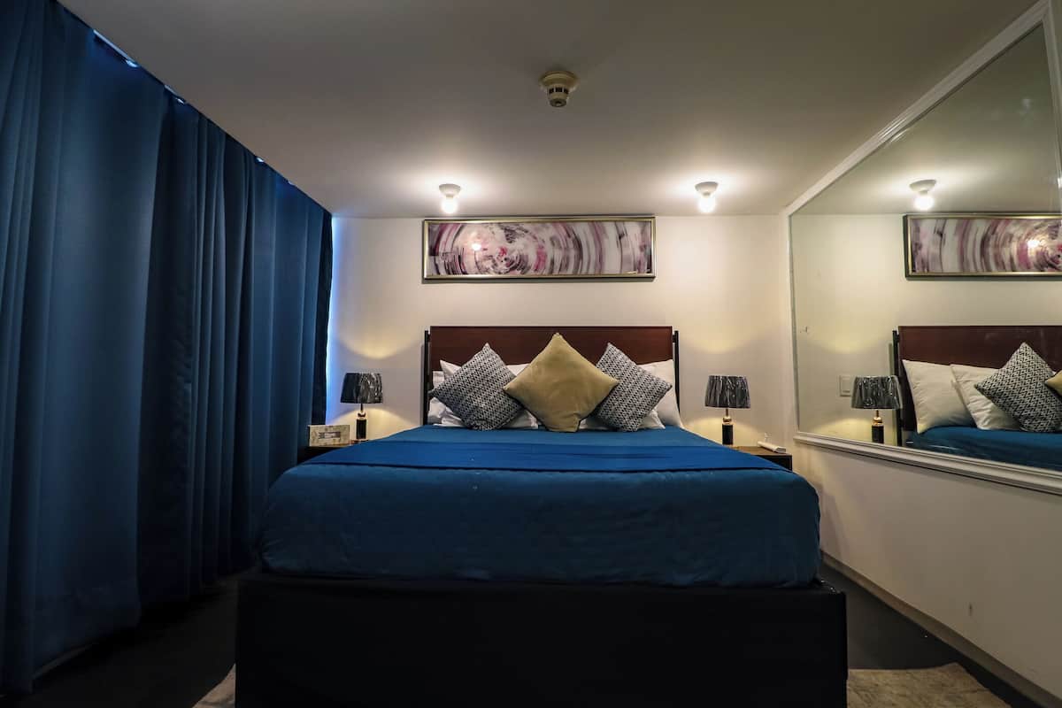 A bedroom with a large bed, two bedside tables with lamps, a mirror, and a painting on the wall.