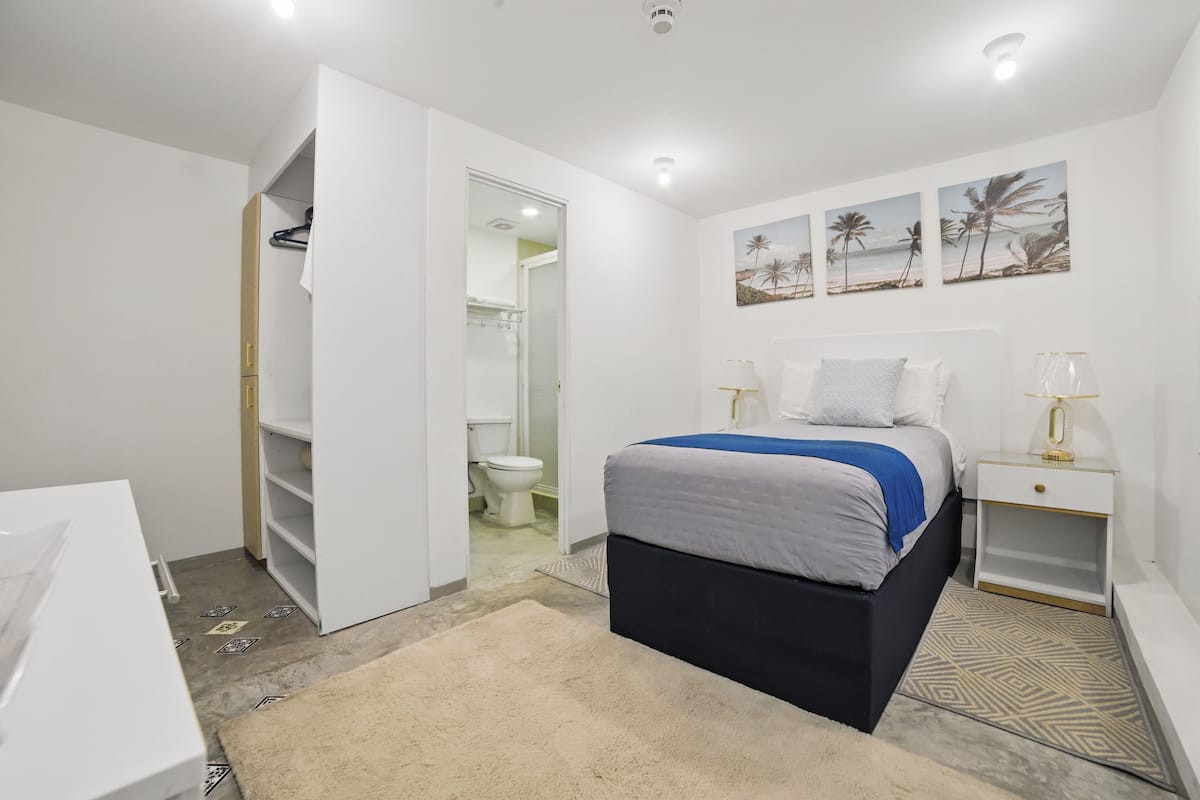 A bedroom with a bed, bedside tables, a wardrobe, and a bathroom visible through an open door.