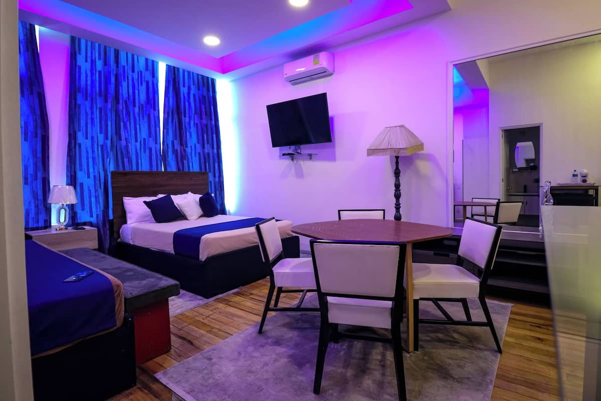 A modern hotel room with a bed, a desk, a chair, a table, and a TV.