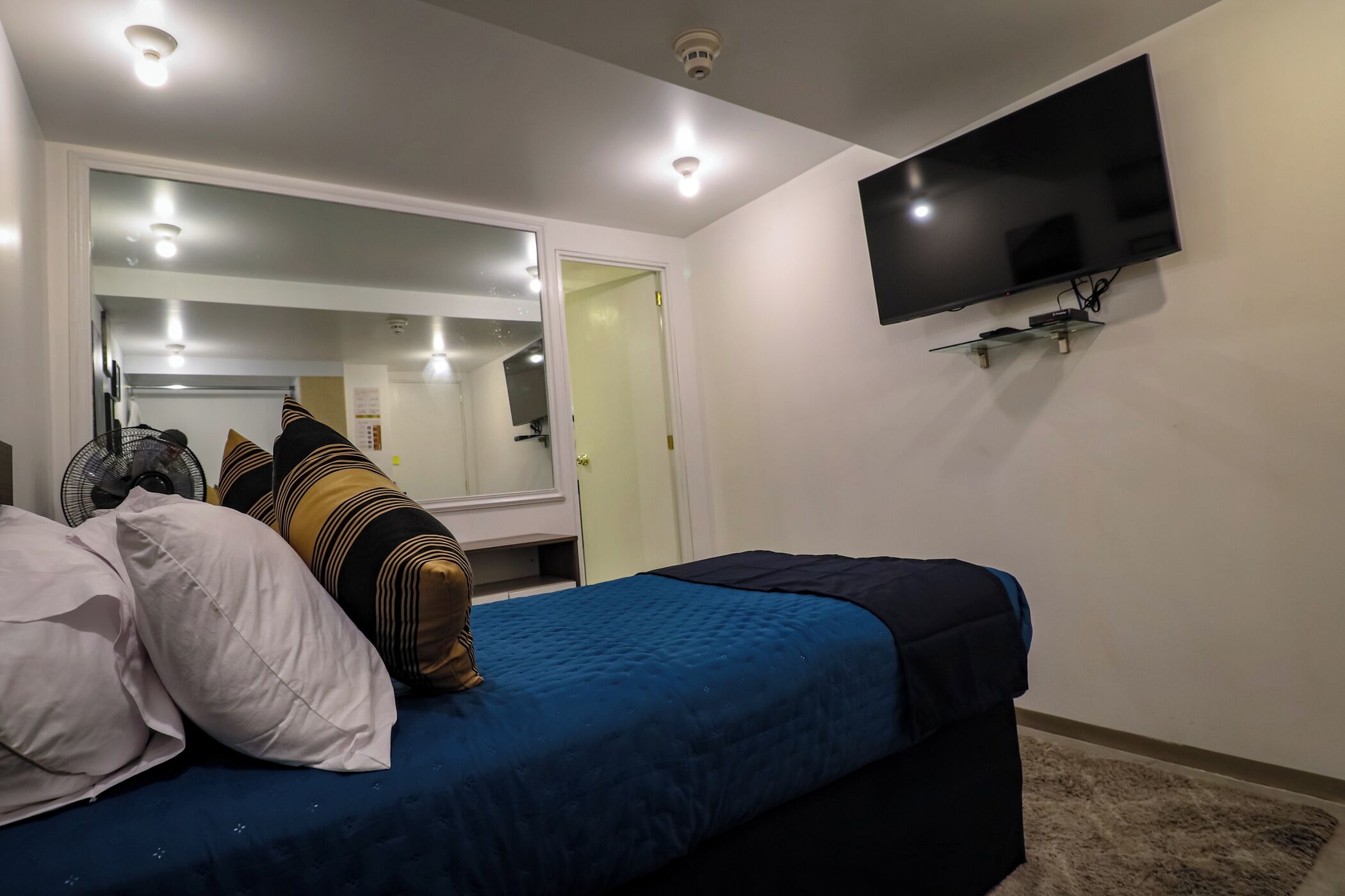 Un dormitorio con cama, televisor montado en la pared y una puerta que da a otra habitación.