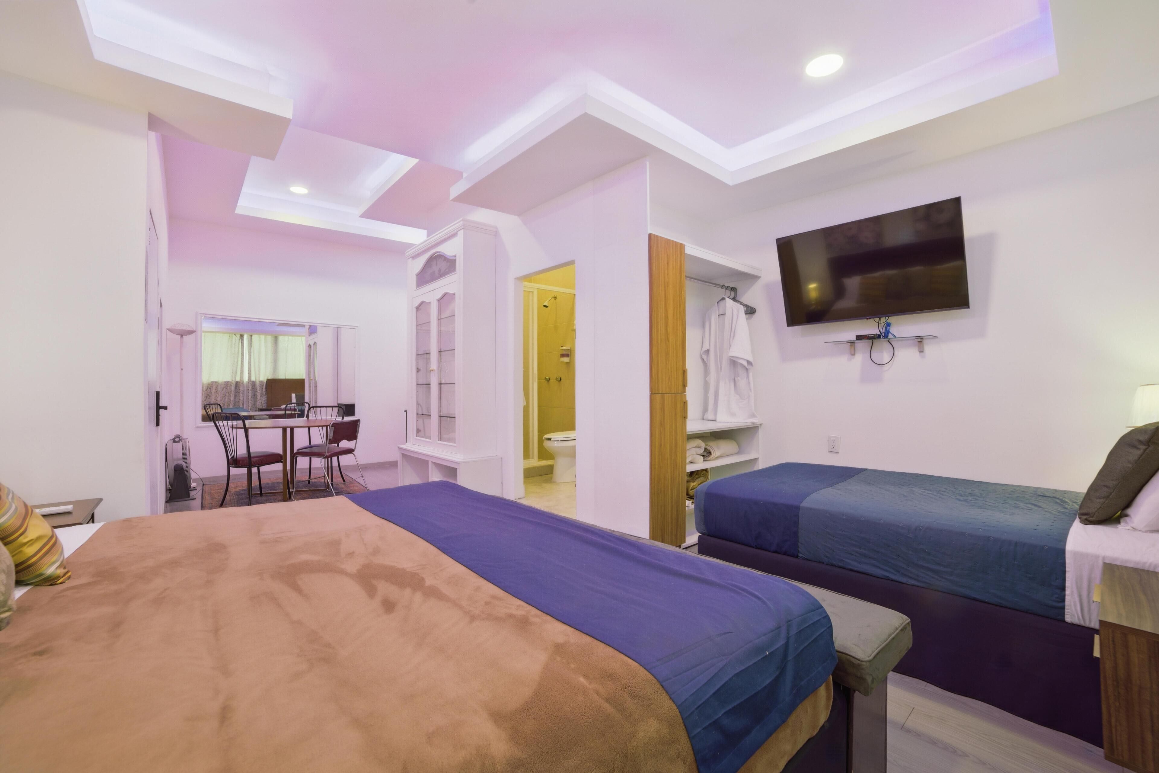 Une chambre d’hôtel avec un grand lit, deux lits simples, une télévision, un bureau avec une chaise et une salle de bain visible à travers une porte ouverte.