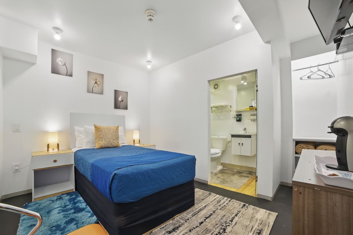 A modern bedroom with a bed, bedside tables, a wardrobe, and a bathroom visible through an open door.