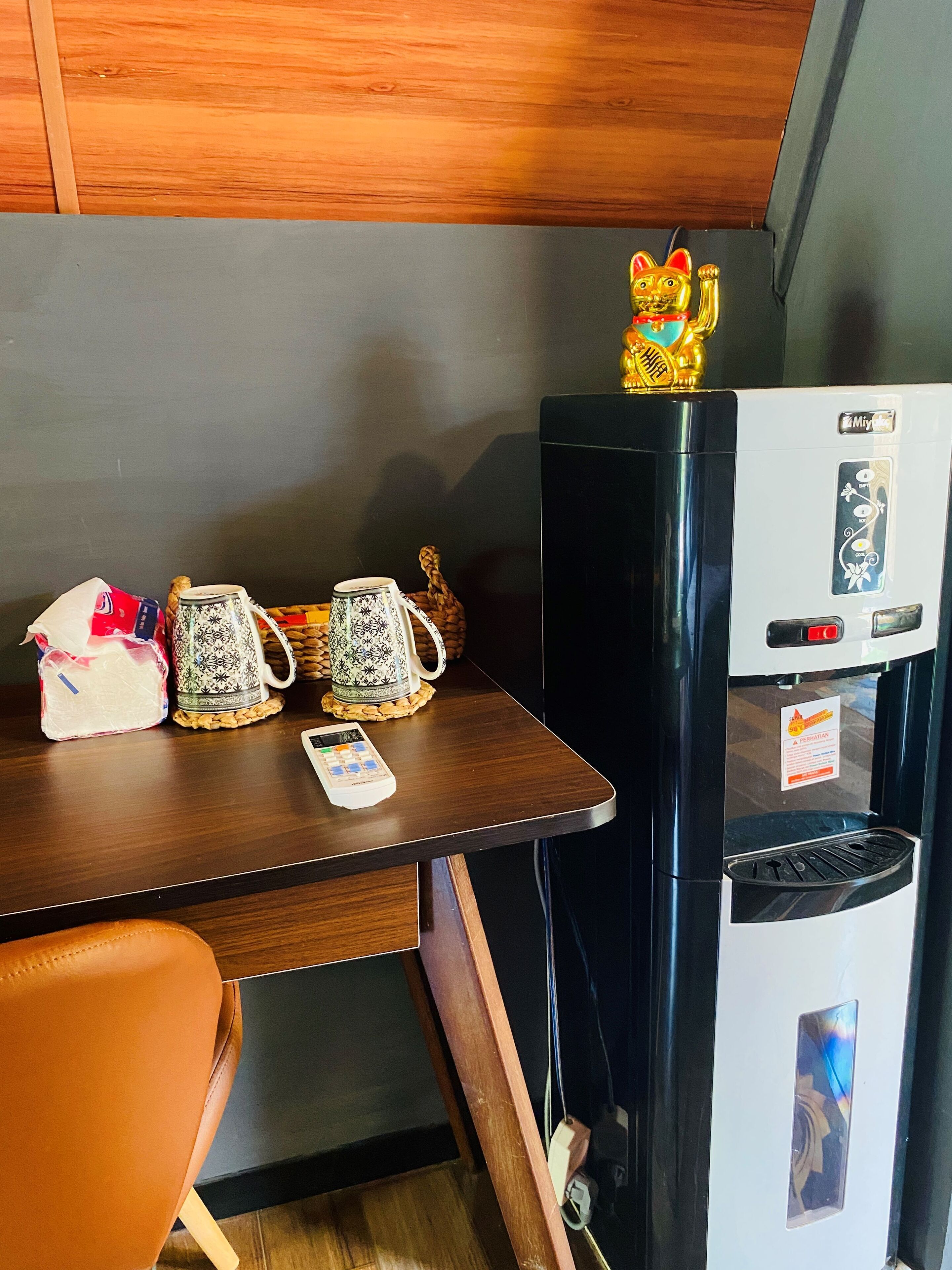 A compact kitchenette with a refrigerator, a coffee maker, a kettle, and a small table.