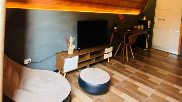Een moderne woonkamer met een schuine plafond, een flatscreen televisie, houten vloer en twee ronde poefs.