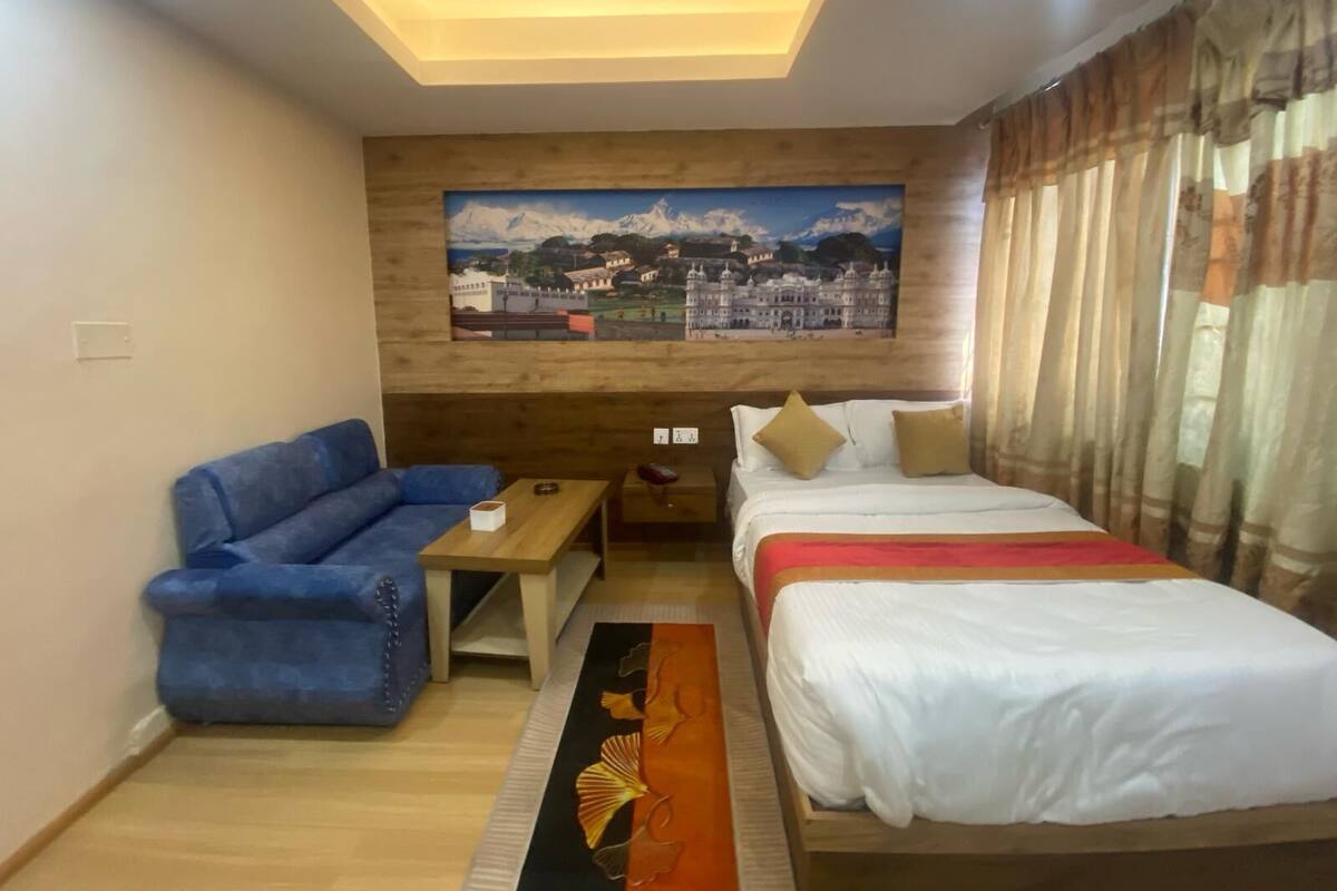 A hotel room with a bed, a blue sofa, a wooden coffee table, and a painting on the wall.