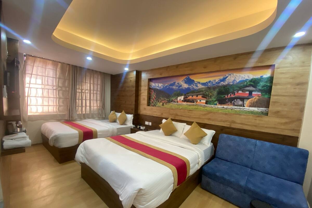 A hotel room with two beds, a blue sofa, a painting of a mountain landscape, and a wooden floor.